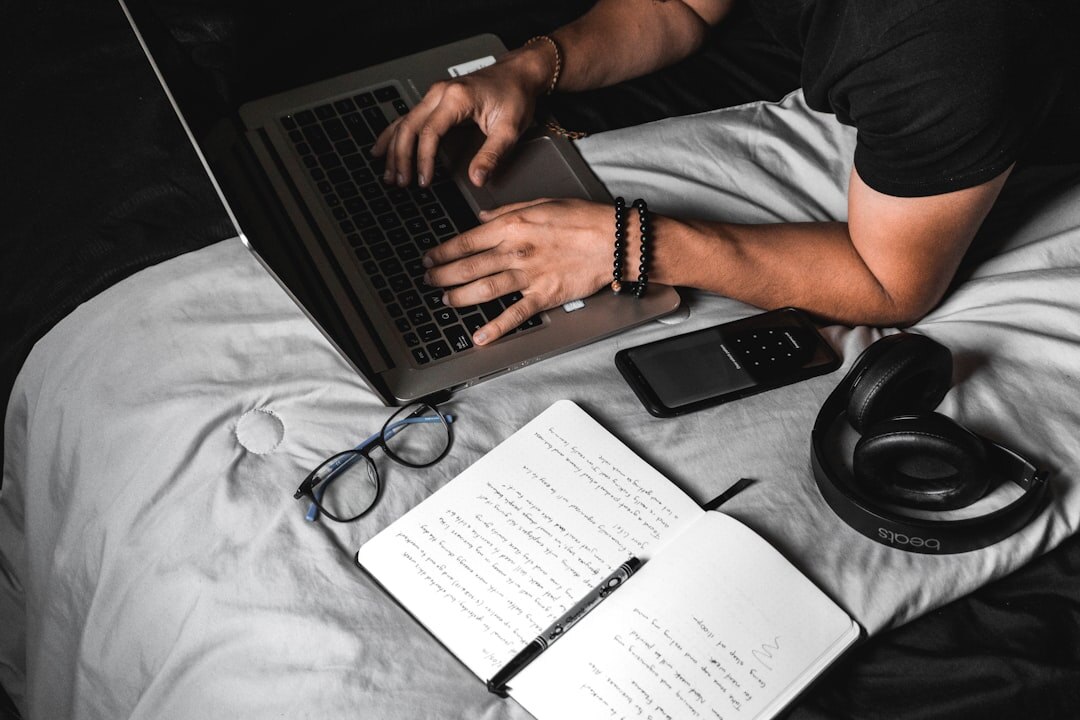 Hands of a brazilian man writing notes and typing on a laptop at a wooden desk